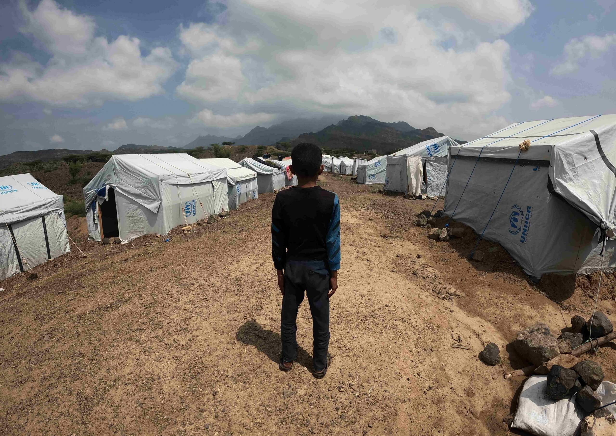 Chlapec hledí na stany v uprchlickém táboře, Jemen.